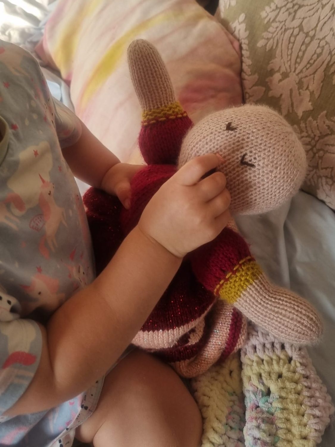 img_2174 Child holding a knitted doll on a bed with patterned and striped pillows